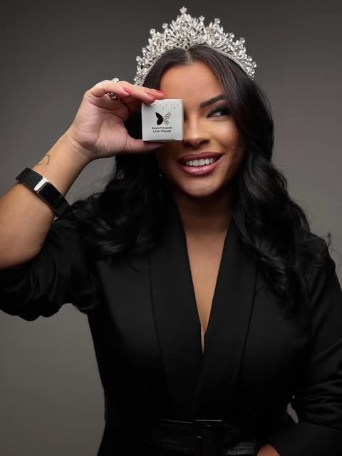 Luana Miranda de coroa, sorrindo, cobrindo um dos olhos com uma caixinha de produto